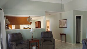 Un salon avec deux fauteuils, une petite table avec une lampe, un meuble et une carte encadrée accrochée au mur.