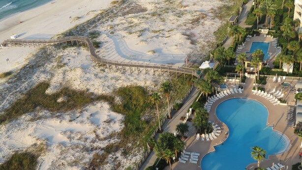 Ein Luftbild eines Resorts mit großem Pool, Strandzugang und verschiedenen Sitzbereichen im Freien.