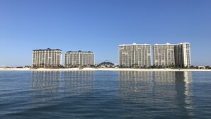 Ein Strandhotel mit mehreren Hochhäusern, einem Sandstrand und ruhigem Wasser, das die Gebäude spiegelt.