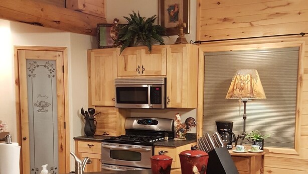 A cozy kitchen with wooden cabinets, a central island with stools, a microwave, and a stove. - Where beautiful scenery is unavoidable! Fly-fishing, hiking/family time w/pets! (Ennis)