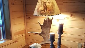 A wooden interior with a table featuring a deer lamp, candles, and a floral arrangement. - Where beautiful scenery is unavoidable! Fly-fishing, hiking/family time w/pets! (Ennis)