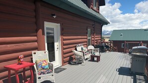 A log cabin with a deck featuring wicker chairs, a red table, and a grill. - Where beautiful scenery is unavoidable! Fly-fishing, hiking/family time w/pets! (Ennis)