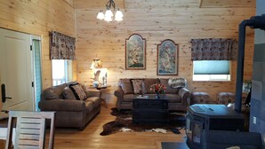 A cozy log cabin interior with a fireplace, two sofas, a coffee table, and decorative wall art. - Where beautiful scenery is unavoidable! Fly-fishing, hiking/family time w/pets! (Ennis)