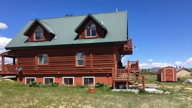 Une cabane en rondins avec un toit en métal vert, un balcon et un petit abri attenant.