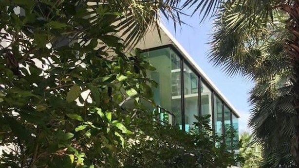 A modern building with large windows, surrounded by lush greenery and a paved walkway. - ICONDO Ngamwongwan 1B by Tanny (Nonthaburi)