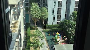 A multi-story residential building with balconies, a central courtyard with palm trees, and a playground. - ICONDO Ngamwongwan 1B by Tanny (Nonthaburi)