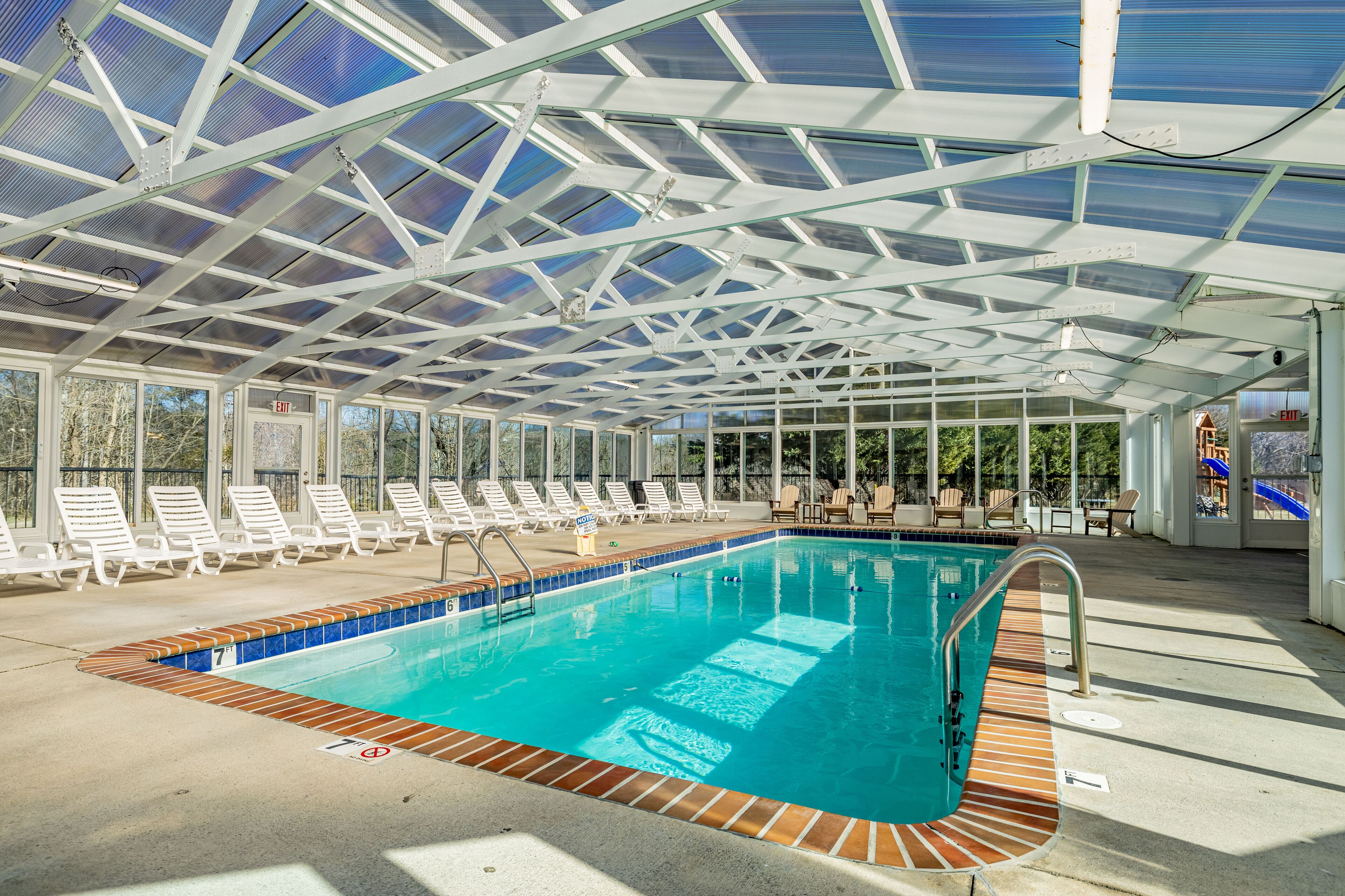 Una piscina techada con sillas de descanso y techo de vidrio.