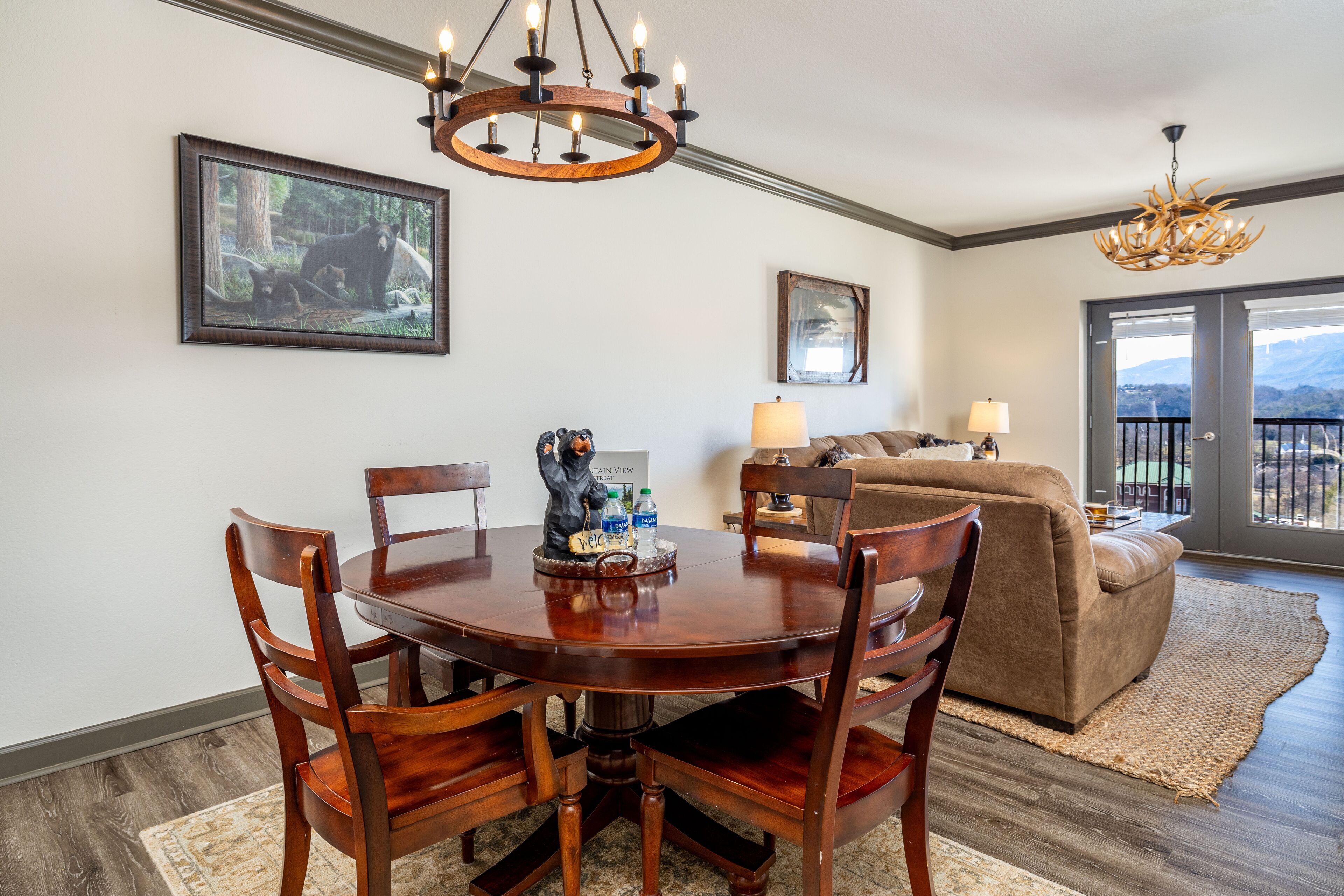 A dining area with a round wooden table and chairs, a chandelier, and a painting on the wall.