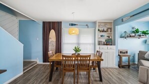 A dining area with a wooden table and chairs, a hanging light fixture, and a window with blinds. - Beachside home in Sea Isle with sunset & waterfront views, 1-min walk to beach! (Galveston)