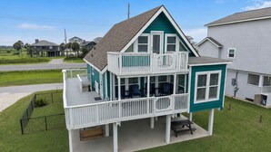 A two-story house with a balcony, a covered porch, and a front yard. - Beachside home in Sea Isle with sunset & waterfront views, 1-min walk to beach! (Galveston)