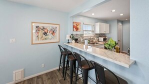 A modern kitchen with a marble countertop, bar stools, and a large window. - Beachside home in Sea Isle with sunset & waterfront views, 1-min walk to beach! (Galveston)