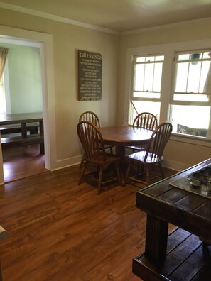A dining area with a wooden table and four chairs, a sign on the wall with table manners, and a window with blinds. - Angler's Retreat near Eufaula Cove (Eufaula)