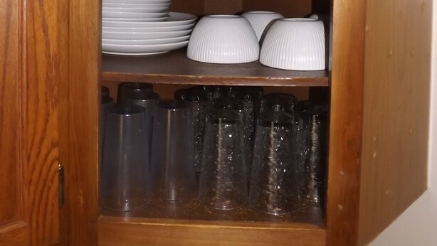 A wooden cabinet with shelves holding white ceramic cups, plates, and glasses.
