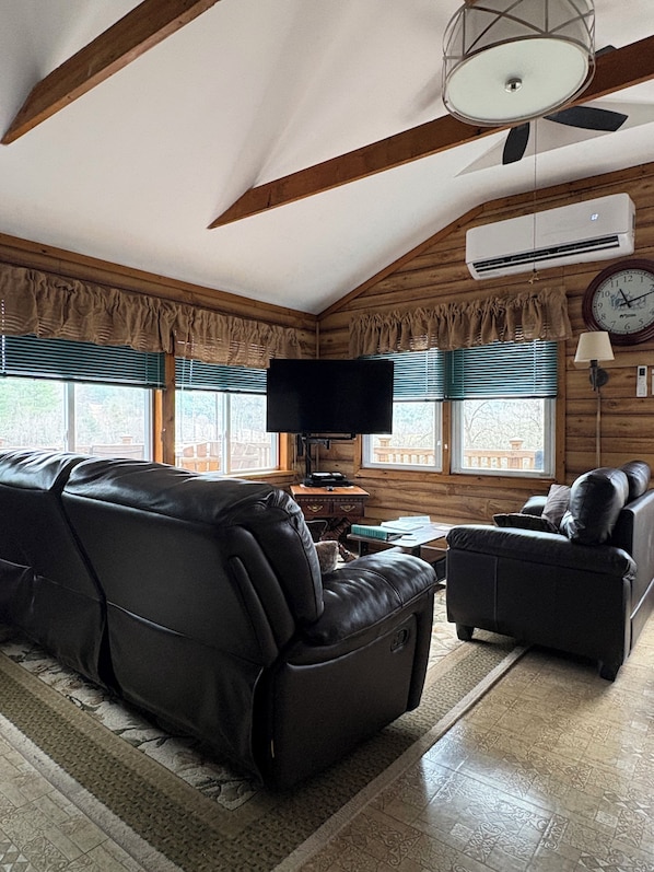 A cozy living room with a sofa, a chair, a flat-screen TV, and a ceiling fan.