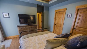 Un dormitorio con cama, almohadas, un televisor sobre un aparador de madera y puertas de madera.