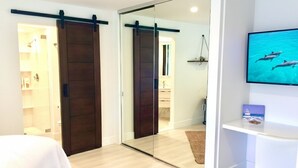 Une chambre d’hôtel avec une porte coulissante, un lit, un téléviseur fixé au mur et une vue sur la mer.