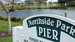 A sign for Northside Park Pier with a view of a lake and trees in the background.