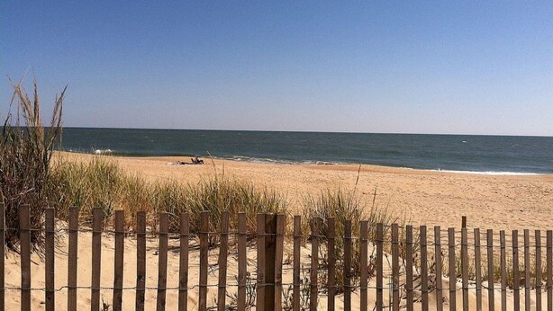 A beach with a wooden fence and sand dunes.