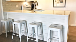 A kitchen with white cabinetry, a white island with stools, a microwave, and a sink.