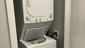 Eine kompakte, weiße Wasch-Trockner-Kombination in einem kleinen Hauswirtschaftsraum mit grauer Wand.