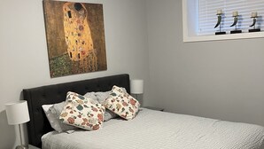 Ein Schlafzimmer mit Bett, Nachttisch, Lampe, einem Gemälde und einem Fenster mit Jalousien.