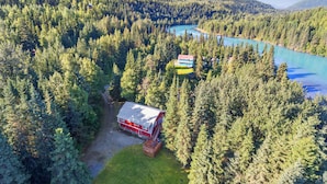 A lodge surrounded by dense forest and a lake, with mountains in the background.