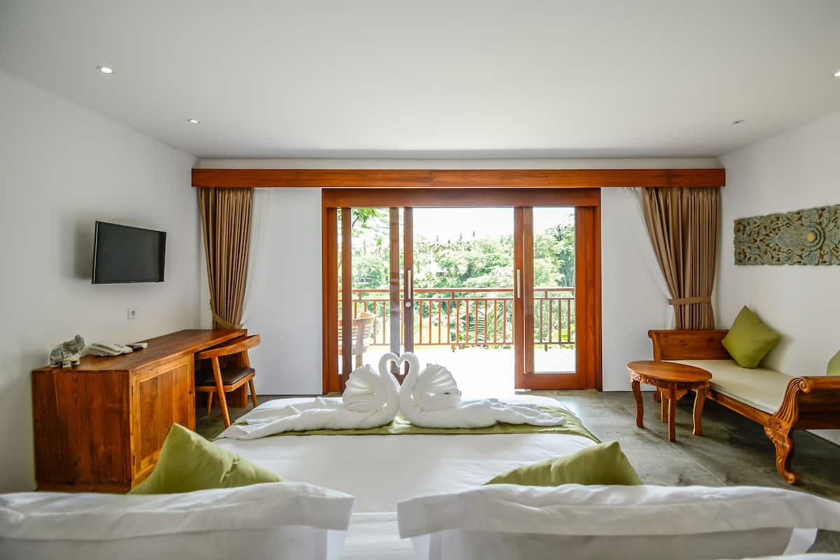 Habitación de hotel con cama, escritorio, televisión y balcón con vista a follaje.