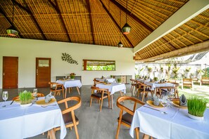 A restaurant with multiple tables, each set with plates, cutlery, and glasses. - The Pandora Hotel (Ubud)