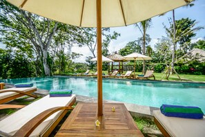 A poolside area with lounge chairs, a wooden deck, and a gazebo in the background. - The Pandora Hotel (Ubud)