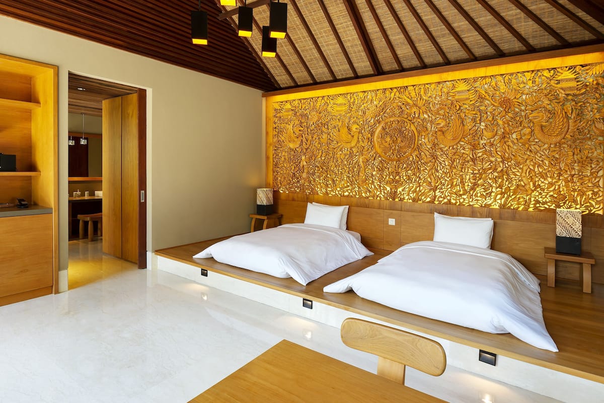 A modern bedroom with a large bed, wooden headboard, and a detailed wall carving.