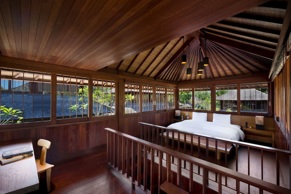 A wooden room with a bed, a desk, and a view of greenery outside.