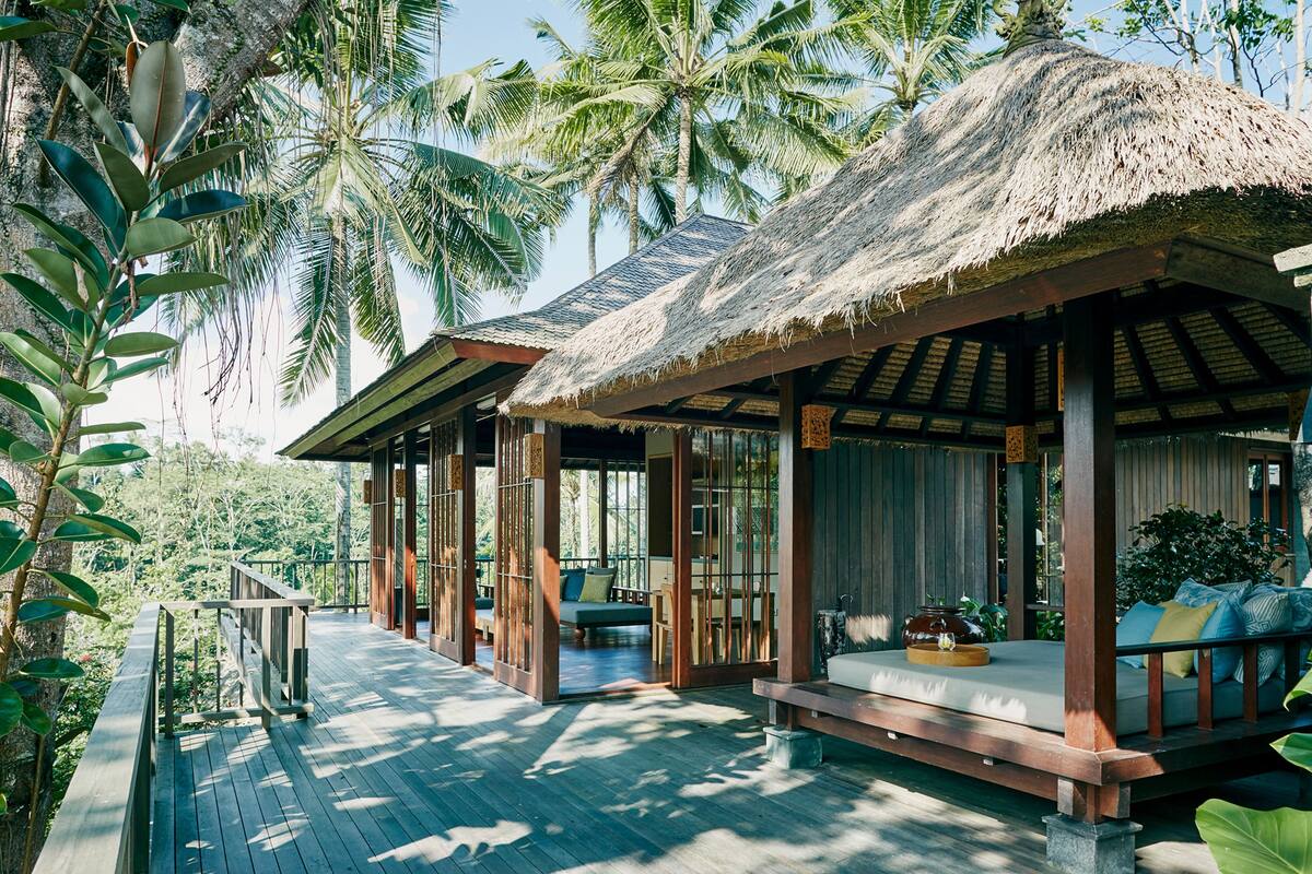 A wooden deck with thatched-roof structures, outdoor seating, and lush tropical vegetation.