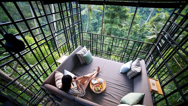 Ein Balkon mit Blick auf einen üppigen Wald, eine gepolsterte Sitzecke mit Kissen und ein Tablett mit Speisen.