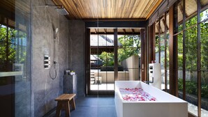 Ein modernes Badezimmer mit einer großen Badewanne, gefüllt mit Rosenblättern, einer Holzbank und einer Duschkabine aus Glas.