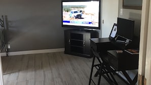 A living room with a flat-screen TV on a stand, a black entertainment unit, and a wooden floor. - No cleaning fee!!!  EV Charging Property in Exclusive Neighborhood! (El Paso)