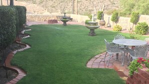 A well-maintained lawn with a patio area featuring a table and chairs, surrounded by decorative plants and a stone wall. - No cleaning fee!!!  EV Charging Property in Exclusive Neighborhood! (El Paso)