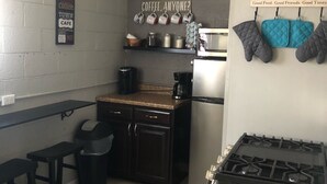 A compact kitchen with a gas stove, a coffee machine, and a small countertop. There are two stools and a shelf with jars and a coffee pot. - No cleaning fee!!!  EV Charging Property in Exclusive Neighborhood! (El Paso)