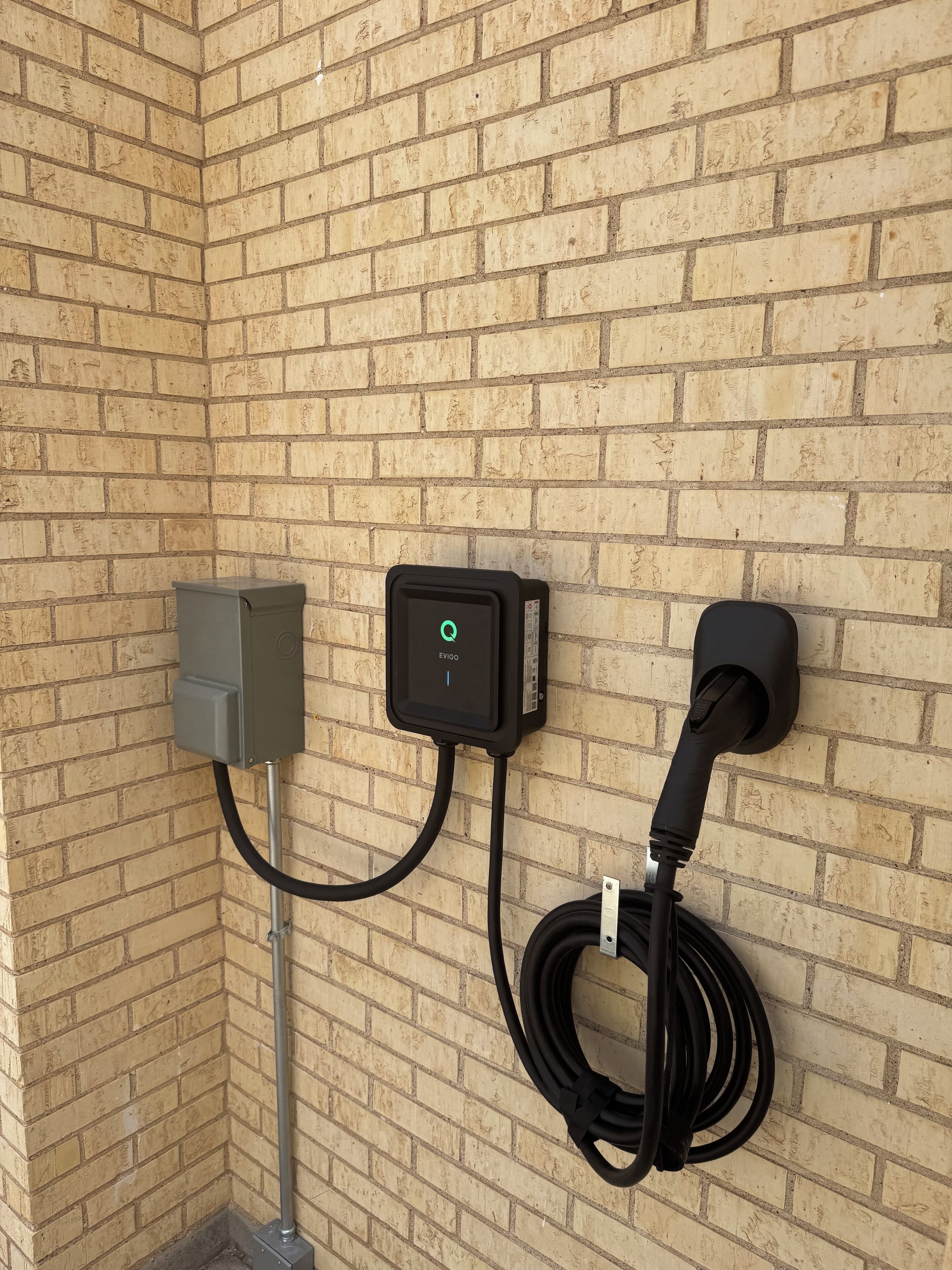Un mur de briques avec une borne de recharge pour véhicules électriques et une prise de courant.