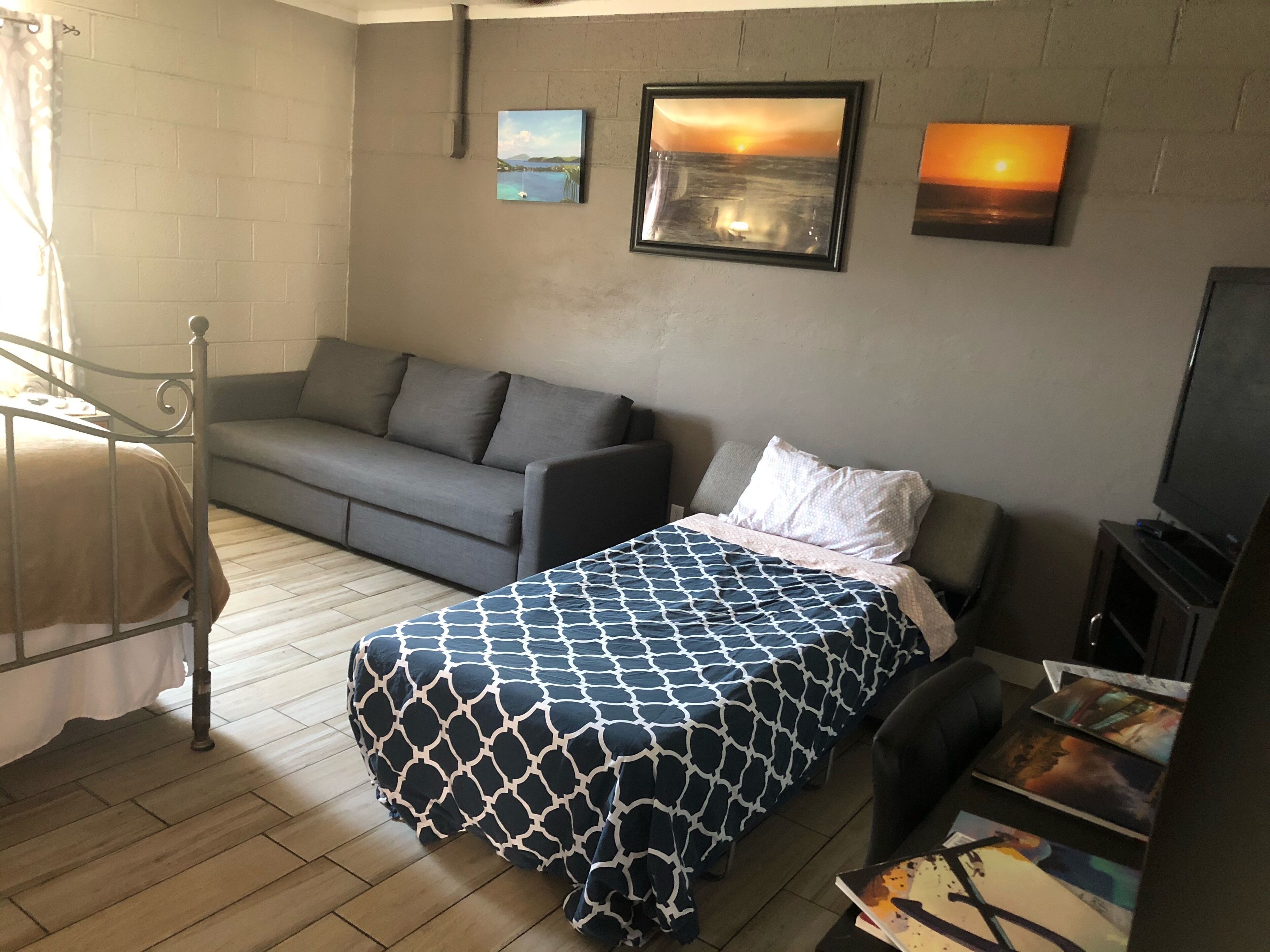 Un dormitorio con cama, sofá, televisión y obras de arte en la pared.
