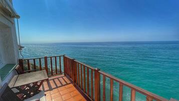 Un balcón con vista al mar, baranda de madera y suelo de baldosas.