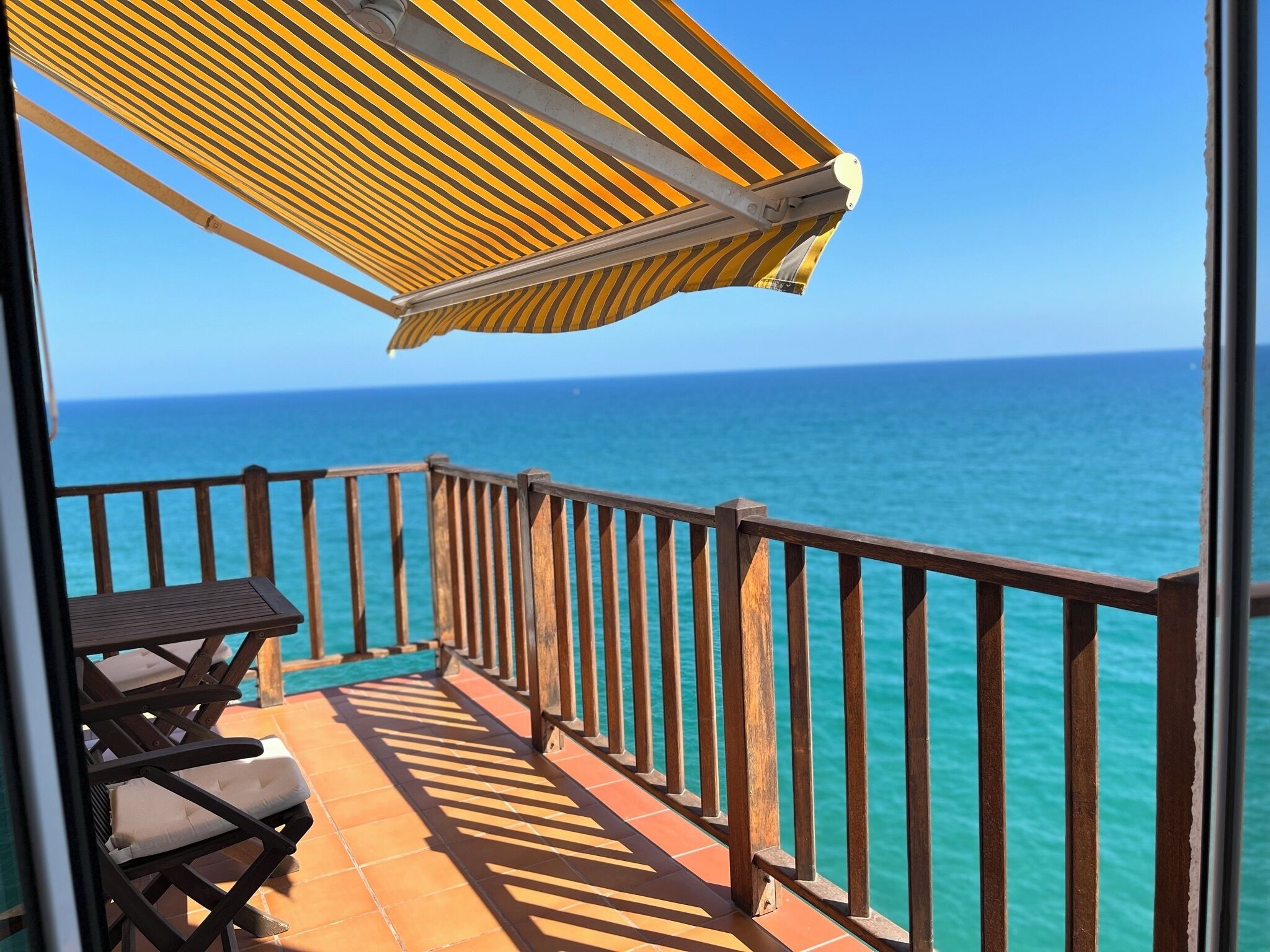 Un balcone con vista sull'oceano, una ringhiera in legno e un tavolo con sedie.
