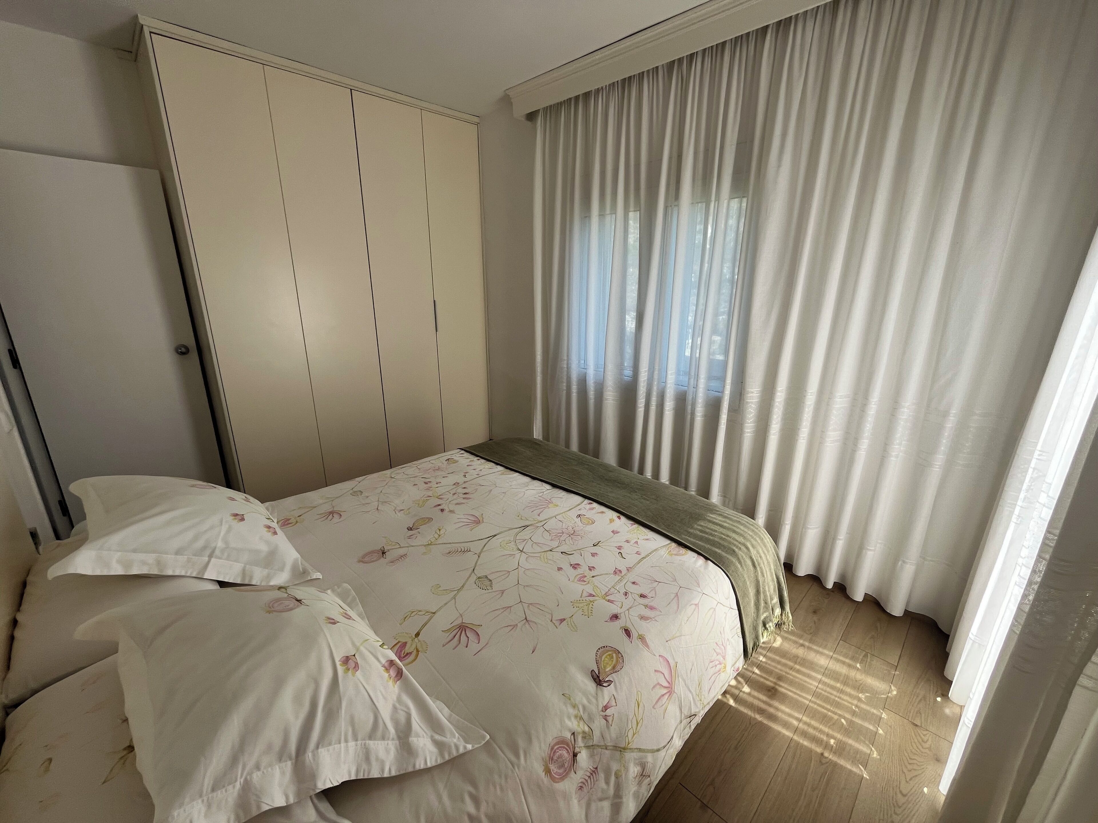 Quarto com cama, guarda-roupa e janela com cortinas.