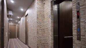 A hallway with a striped carpet, stone wall, and an elevator with a digital display. - A Ace Hotel (Taichung)