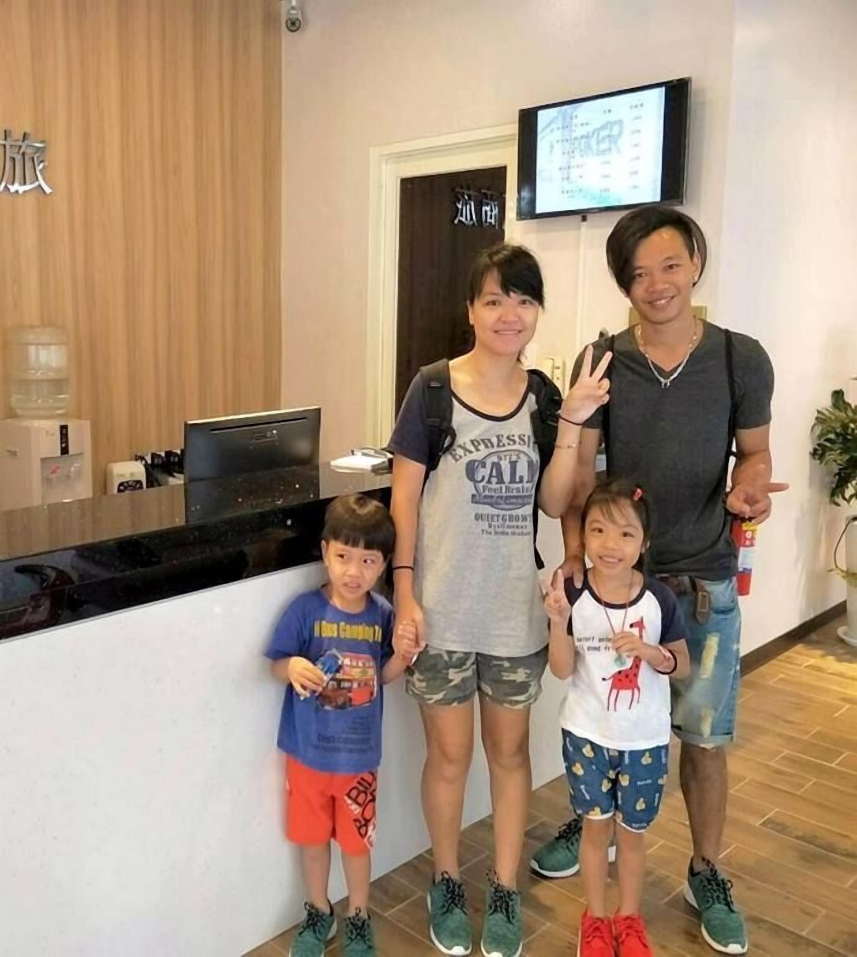 A family of four in a hotel lobby with a reception desk, a television screen, and a water dispenser.