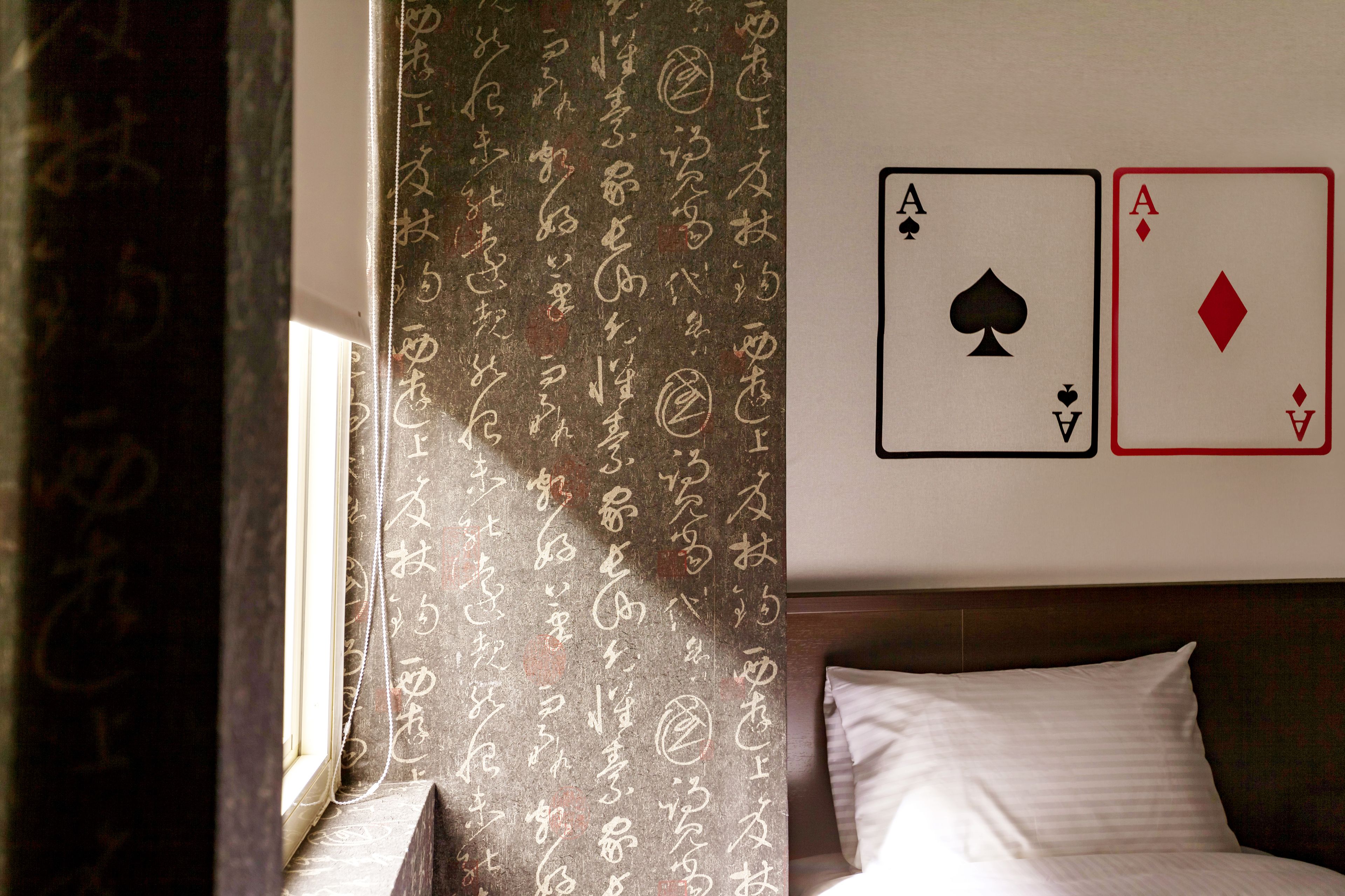 A hotel room with a bed, a window with curtains, and two playing cards (Ace of Spades and Ace of Diamonds) on the wall.