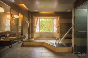 Een moderne badkamer met een ruime badkuip, een aparte douche en een raam met gordijnen.