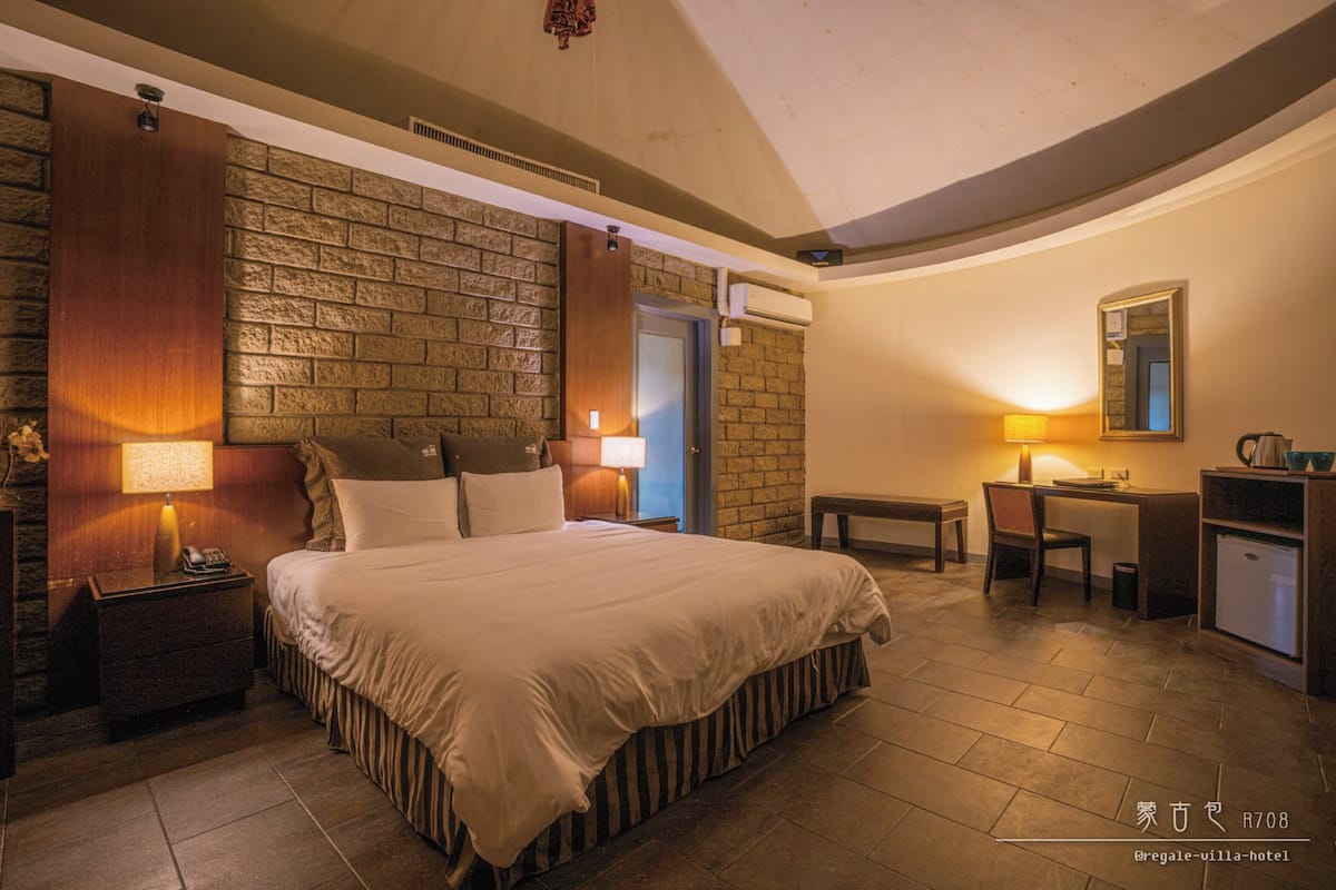 Een hotelkamer met een groot bed, een bureau en een kleine kitchenette.