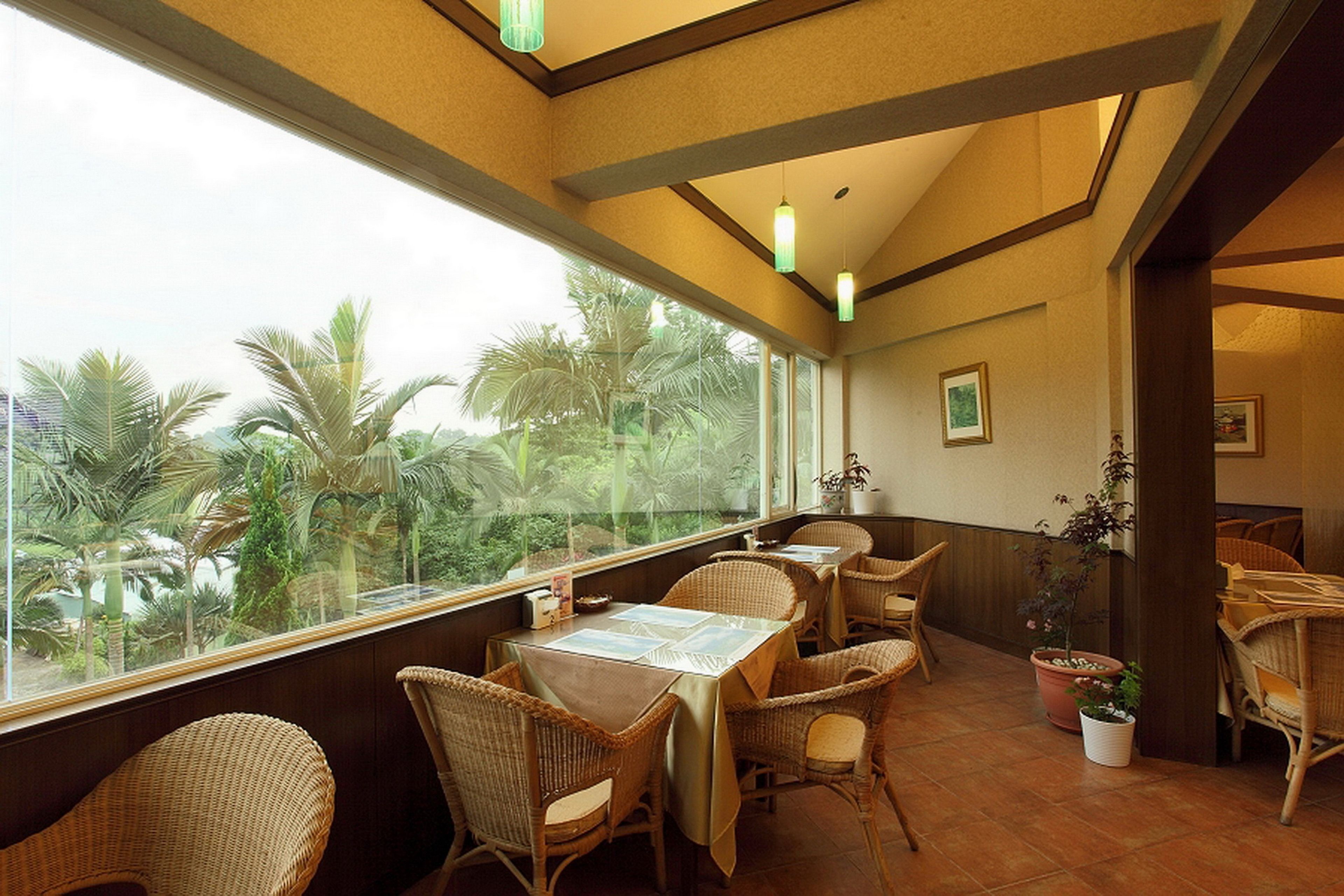 A restaurant with wicker furniture and large windows overlooking palm trees.