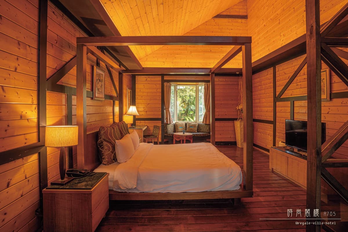 Een slaapkamer in chaletstijl met een bed, nachtkastje, lamp en een televisie.