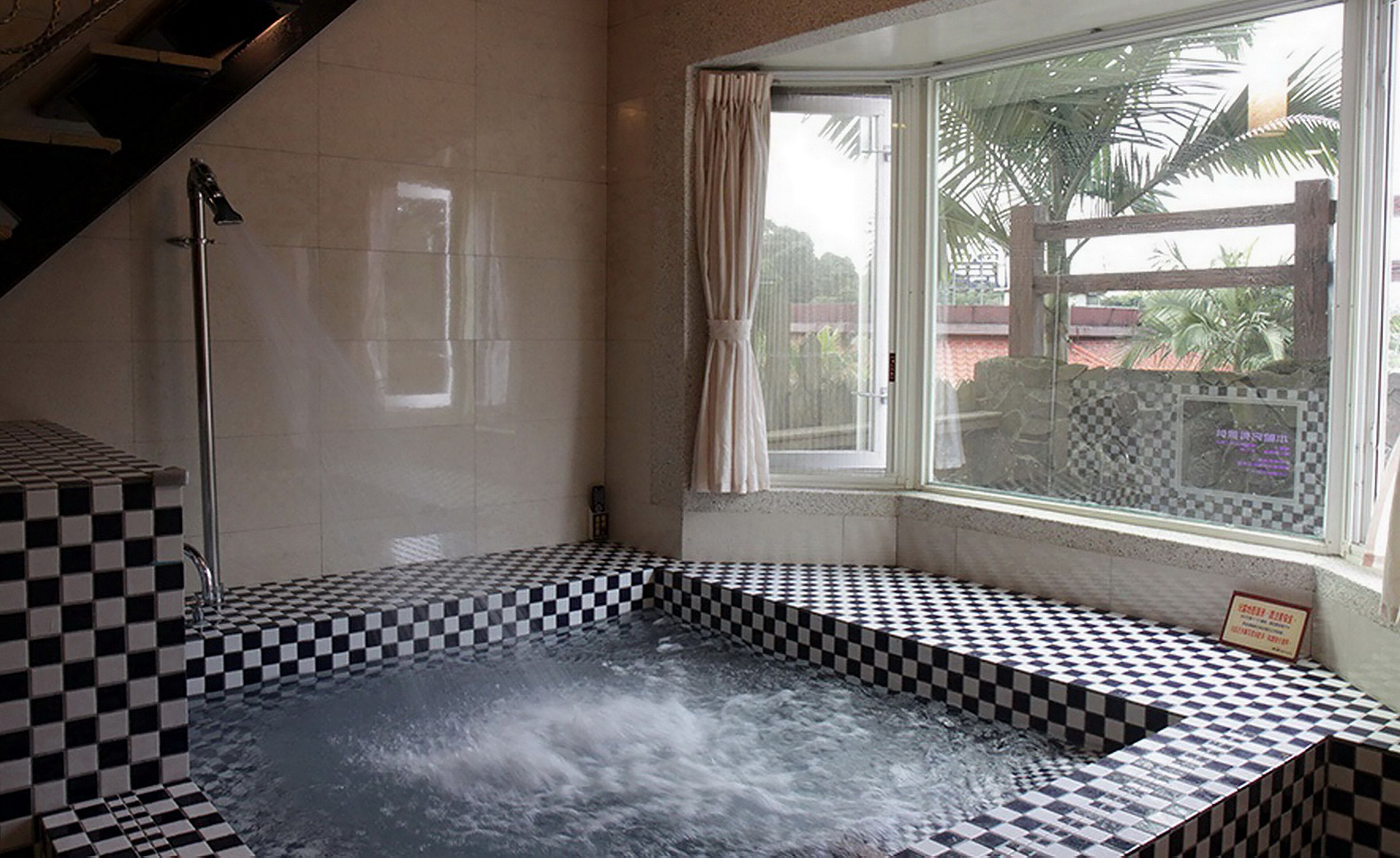 A hot tub with checkered tiles, a shower, and a window with curtains.